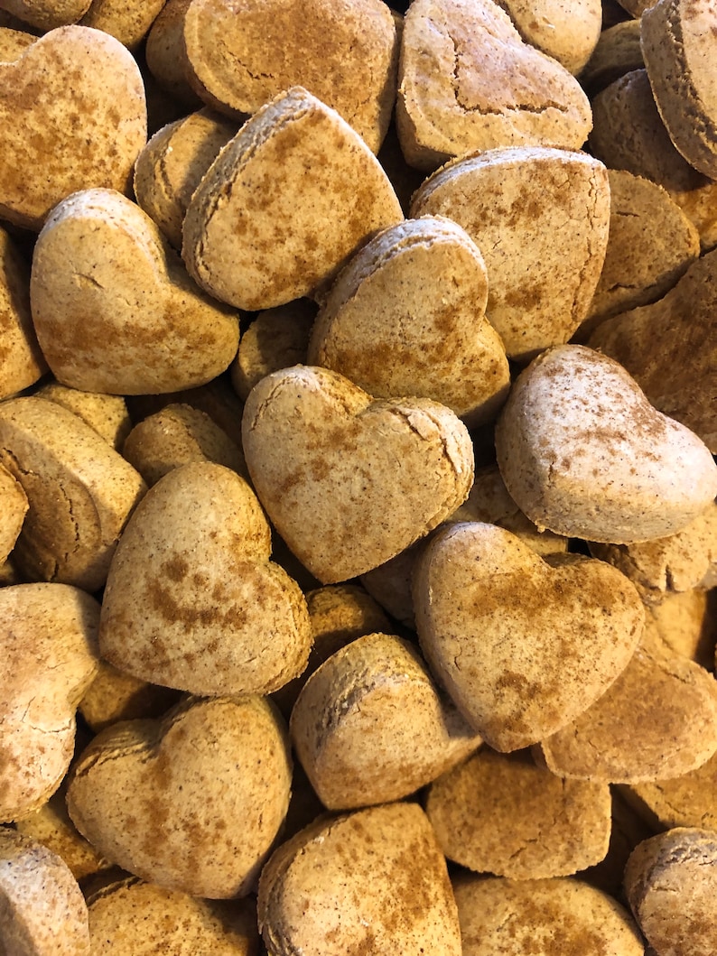 K&ouml;nnte beinhalten: Ein Nahaufnahmebild eines Stapels herzf&ouml;rmiger Kekse. Die Kekse sind hellbraun und haben eine leicht raue Textur. Sie scheinen hausgemacht zu sein und haben ein rustikales Aussehen.