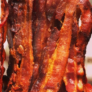 May include: Close-up of crispy, golden brown bacon strips. The bacon is cooked to perfection, with a slightly caramelized exterior and a juicy interior.