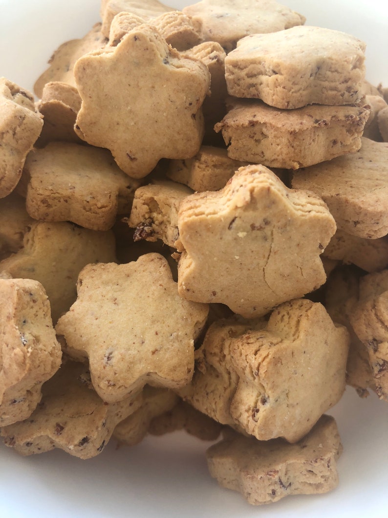 May include: A close-up shot of a pile of star-shaped cookies. The cookies are a light brown color with a slightly rough texture. Some cookies have visible dark specks, possibly from added ingredients. The cookies are stacked together, filling the frame.