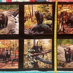 May include: A black fabric panel with six squares featuring black bears in a forest setting. Each square has a different scene with a bear or bears in a forest setting. The bears are brown and black and are in various poses. The fabric is black with a brown border around each square.