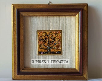 Op de afbeelding: Een ingelijst mozaïekkunstwerk dat een gestileerde boom in tinten geel en oranje voorstelt. De lijst is goudkleurig met een donkerbruine binnenrand. De tekst "3 PINZE 1 TENAGLIA" is onder het kunstwerk gedrukt.