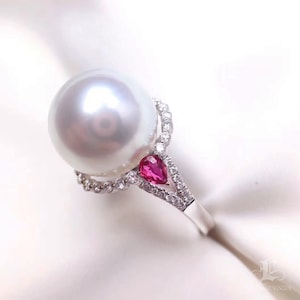 May include: A white pearl ring with a pear-shaped ruby and diamond accents. The ring is set in silver.