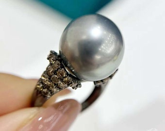 Pode incluir: Um anel de prata com uma grande pérola cinza e um aglomerado de pequenos diamantes engastados na banda.