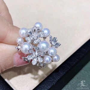May include: A delicate pearl and diamond floral brooch. The brooch features a cluster of white pearls arranged in a flower shape, with diamond accents.