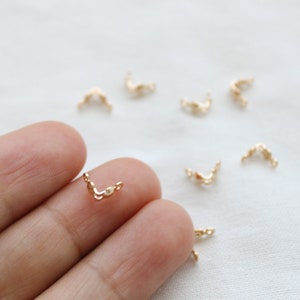 May include: Gold-toned metal chain connectors, shaped like a V, for jewelry making. The connectors are small and delicate, and there are several of them scattered on a white surface.