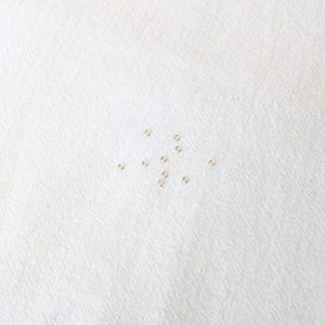 May include: A collection of small, gold jump rings scattered on a white fabric surface.