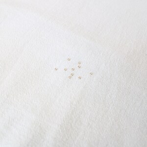 May include: A close-up of a white surface with a scattering of small, gold jump rings.
