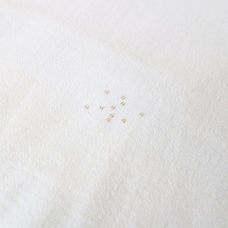 May include: A close-up of a white surface with a scattering of small, gold jump rings.