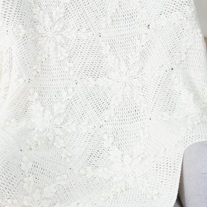 White crochet blanket with snowflake motifs laying over a chair.