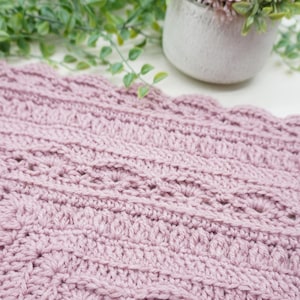 Pink, textured crochet blanket next to some greenery.