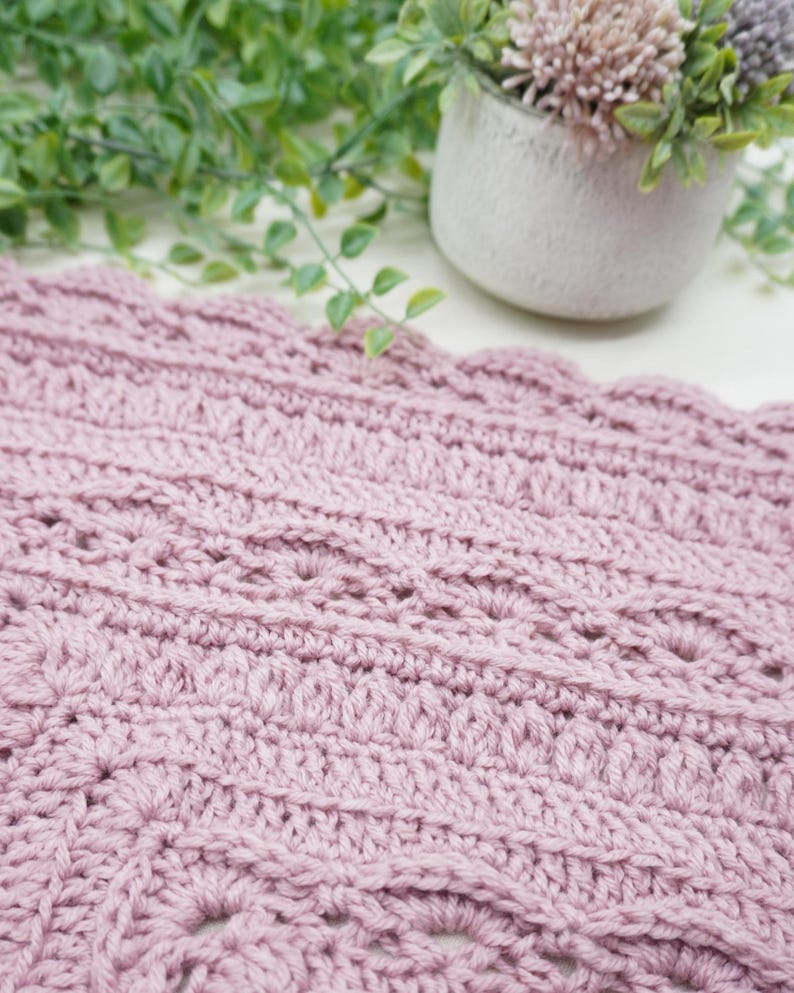 Pink, textured crochet blanket next to some greenery.
