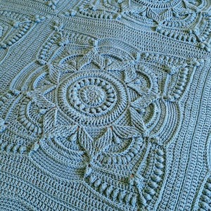 Crochet blanket laying on queen-sized bed.