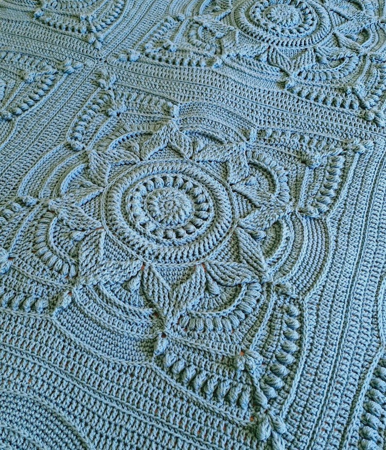 Crochet blanket laying on queen-sized bed.