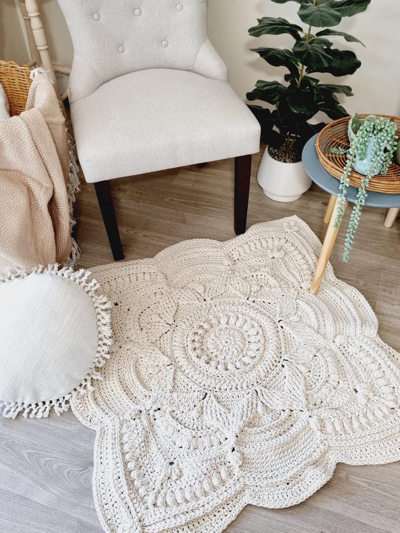 White, square crochet floor rug in front of a chair, cushion, coffee table and plant.
