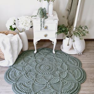 Floral, green crochet floor rug in front of a white set of drawers and a blanket basket.