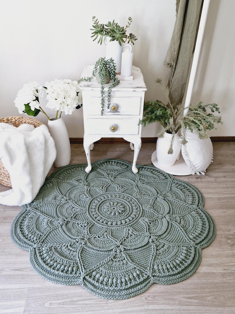 Floral, green crochet floor rug in front of a white set of drawers and a blanket basket.