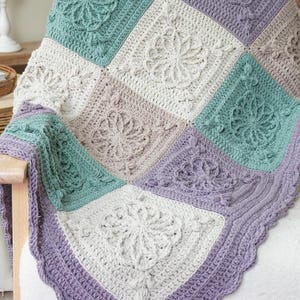May include: A handcrafted crochet blanket in a patchwork design. The blanket features squares in shades of teal, lavender, cream, and taupe, with floral and geometric patterns. The border is a scalloped edge in a lavender hue.