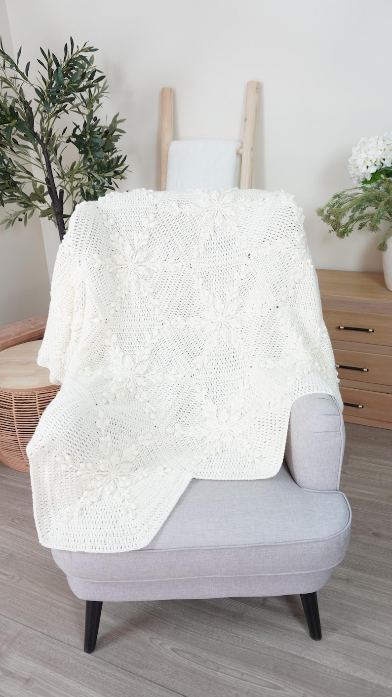 White crochet blanket with snowflake motifs laying over a chair.