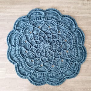 May include: A round, blue crocheted rug with a detailed, mandala-like design. The rug features a scalloped edge and intricate patterns, including openwork and raised textures. The rug is approximately 91 cm in diameter.
