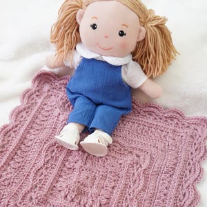 Pink crochet blanket with a doll sitting on the edge.