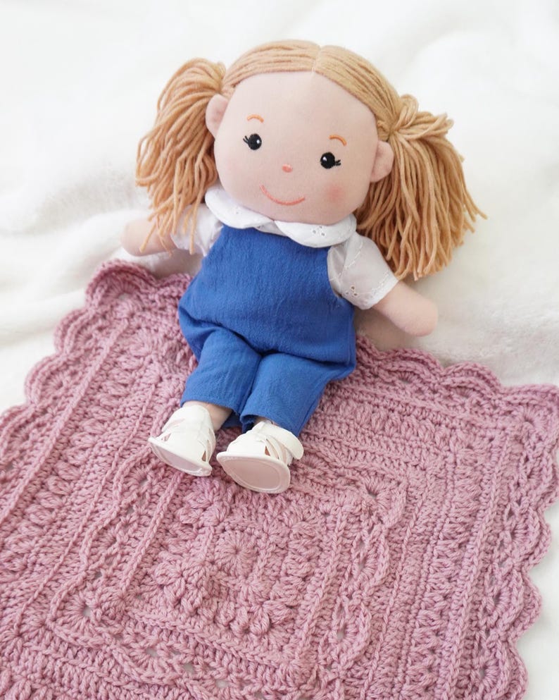 Pink crochet blanket with a doll sitting on the edge.