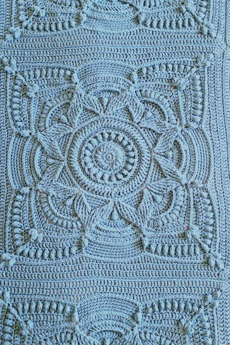 Crochet blanket laying on queen-sized bed.