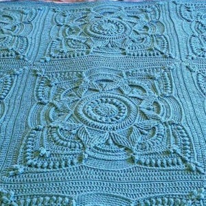 Crochet blanket laying on queen-sized bed.