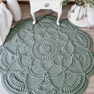 Floral, green crochet floor rug in front of a white set of drawers and some plants.