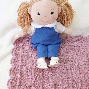 Crochet blanket with a doll sitting on the edge.