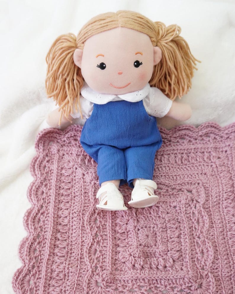 Crochet blanket with a doll sitting on the edge.