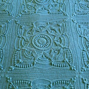 Crochet blanket laying on queen-sized bed.