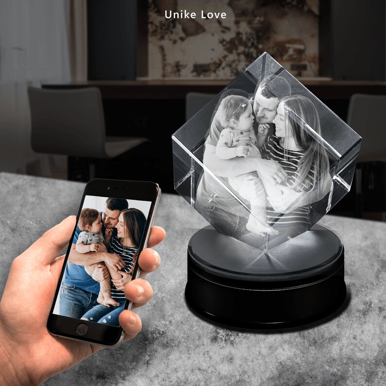 K&ouml;nnte beinhalten: Ein klarer Kristallw&uuml;rfel mit einem Familienfoto, auf einem schwarzen, rotierenden Sockel. Ein Smartphone zeigt dasselbe Bild. Der Text "Unike Love" ist oben links zu sehen.