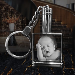 May include: A silver keychain with a crystal cube charm. The cube contains a black and white photo of a baby sleeping.