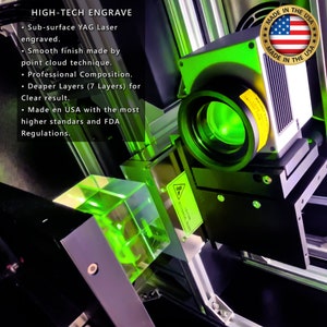 Puede incluir: Primer plano de una m&aacute;quina de grabado de alta tecnolog&iacute;a con un rayo l&aacute;ser verde enfocado en un bloque de vidrio transparente. La m&aacute;quina est&aacute; etiquetada como "HIGH-TECH ENGRAVE" y "MADE IN THE USA".