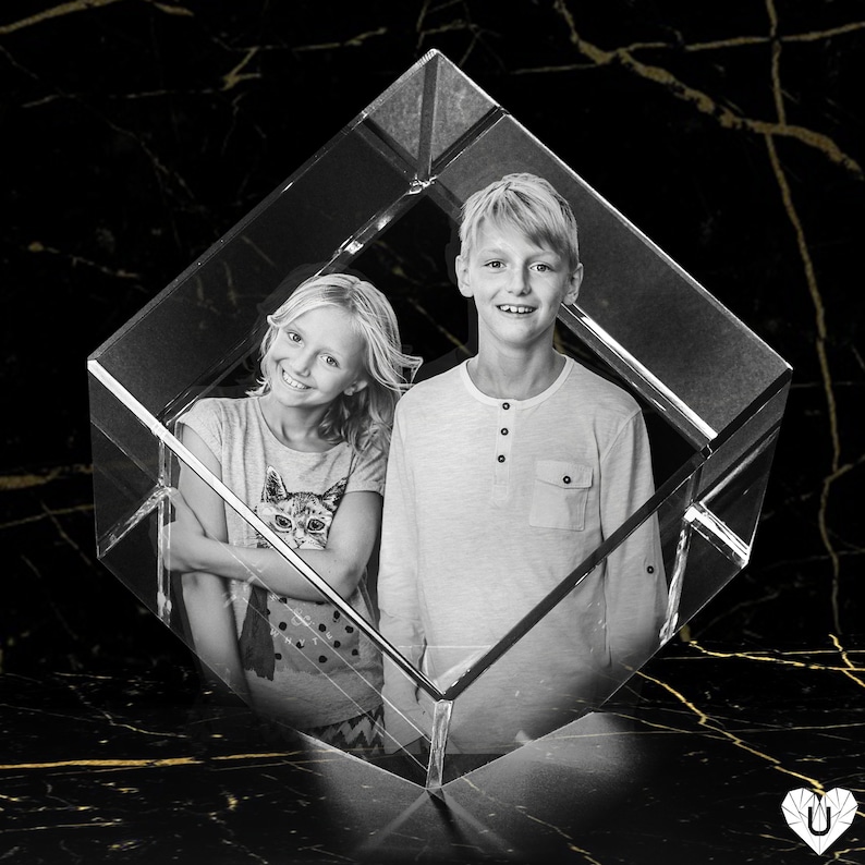 K&ouml;nnte beinhalten: Schwarz-Wei&szlig;-Fotografie von zwei l&auml;chelnden Kindern in einem transparenten, geometrischen Prisma. Das M&auml;dchen tr&auml;gt ein T-Shirt mit einem Katzenmotiv. Der Junge tr&auml;gt ein lang&auml;rmliges Hemd. Der Hintergrund ist schwarz mit goldenen Adern.
