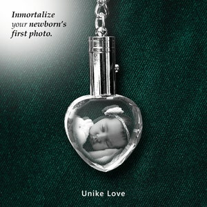 May include: A silver heart-shaped crystal keychain with a photo of a sleeping baby inside. The keychain has a silver chain and a silver cap on top. The text "Unike Love" is printed below the crystal.