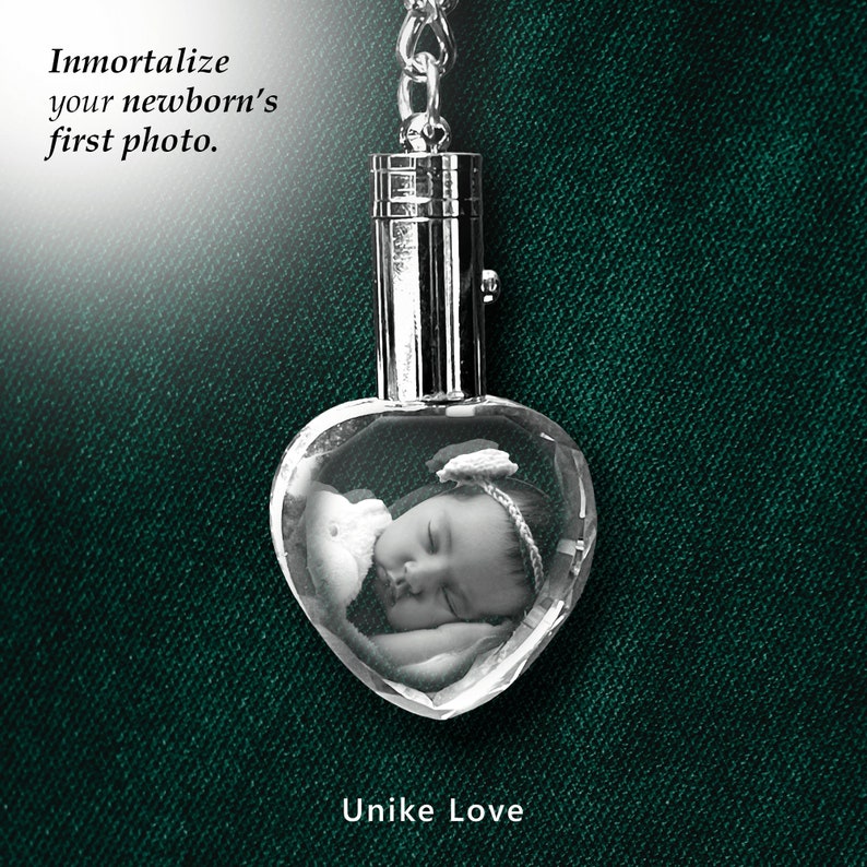 May include: A silver heart-shaped crystal keychain with a photo of a sleeping baby inside. The keychain has a silver chain and a silver cap on top. The text "Unike Love" is printed below the crystal.