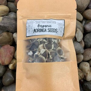 May include: A brown paper pouch with a clear window, containing organic moringa seeds. The pouch has a label that reads "#healthyvibration heal-thy-vibe.com Organic Moringa Seeds".