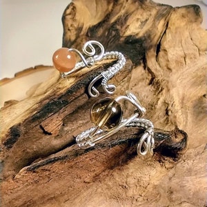 Puede incluir: Dos anillos envueltos en alambre con cuentas de piedras preciosas. El anillo superior tiene una cuenta de color naranja claro y el anillo inferior tiene una cuenta de color marr&oacute;n.