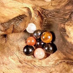 Puede incluir: Una colecci&oacute;n de ocho cuentas redondas de piedras preciosas en varios colores, incluyendo negro, marr&oacute;n, rojo, blanco y beige. Las cuentas est&aacute;n dispuestas en un grupo sobre una pieza de madera.