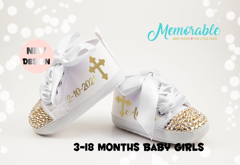 Pode incluir: Sapatos de beb&eacute; brancos com detalhes de glitter dourado e um design de cruz dourada. Os sapatos t&ecirc;m uma fita de cetim branca e o texto "2-10-2021" est&aacute; impresso em um sapato. Os sapatos s&atilde;o para beb&eacute;s de 3 a 18 meses.