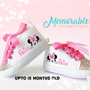 May include: White baby shoes with pink polka dot laces and a Minnie Mouse graphic. The shoes have a rhinestone-studded toe and the name "Alice" printed on the side. The text "Memorable BABY SHOES FOR LITTLE ONES" and "UPTO 18 MONTHS OLD" are also visible.