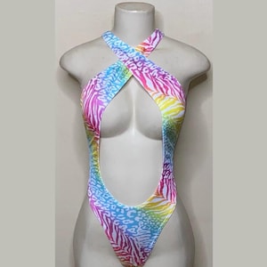 May include: A colorful one-piece swimsuit with a halter neckline and a high-cut leg. The swimsuit features a vibrant pattern of zebra stripes and leopard spots in shades of pink, blue, yellow, and white. The garment is displayed on a mannequin.