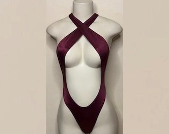 May include: A deep burgundy bodysuit featuring a high-cut leg design and a halter neckline with fabric straps that cross over the chest, creating a large cutout detail that extends from the neck down to the waistline on a mannequin.