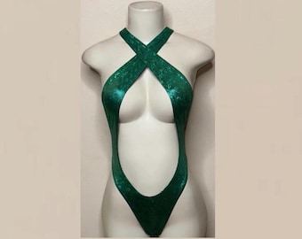 Può includere: Un body verde smeraldo metallizzato caratterizzato da un taglio sgambato e uno scollo all'americana con ampie spalline che si incrociano sul petto, creando un'ampia apertura centrale che va dallo scollo fino alla zona della vita.