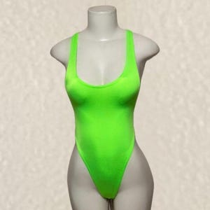 May include: A neon green one-piece swimsuit featuring a high-cut leg design, a deep scoop neckline, and wide shoulder straps. The garment is displayed on a mannequin, showcasing a solid, vibrant color and a smooth, form-fitting fabric construction.