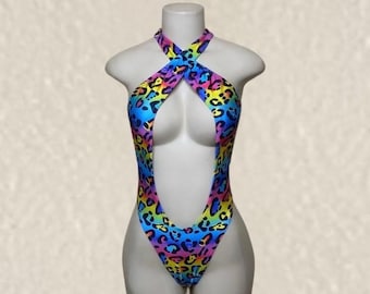 May include: A one-piece swimsuit featuring a vibrant rainbow gradient background with a black leopard print pattern. The garment has a high-cut leg design, a deep plunging front cutout, and a halter-style neckline with crossed straps at the chest.