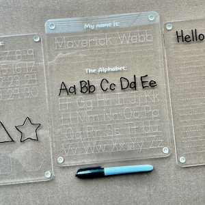 May include: Three clear plastic dry-erase boards with black marker writing. The first board has numbers 1-30, shapes, and a triangle and star. The second board has the alphabet, with the first five letters written in large letters. The third board has the words "Hello there." written on it.