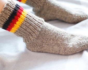 May include: A pair of gray wool socks with a red, yellow, and black stripe pattern. The socks are knitted and have a soft, cozy texture.