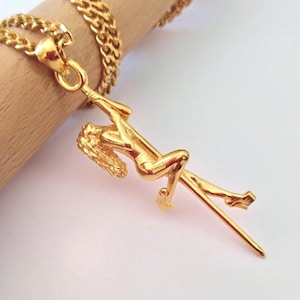 Può includere: Collana con pendente dorato raffigurante una donna su un palo. Il pendente è sospeso a una catena d'oro. La donna è in posa, con una gamba tesa e le braccia attorno al palo.